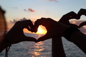 Hands making heart shapes with sunset in the background