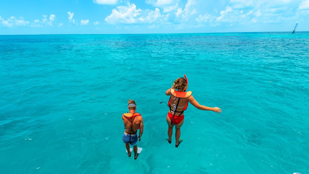 two people jumping in to the crystal blue key west waters wearing snorkel gear
