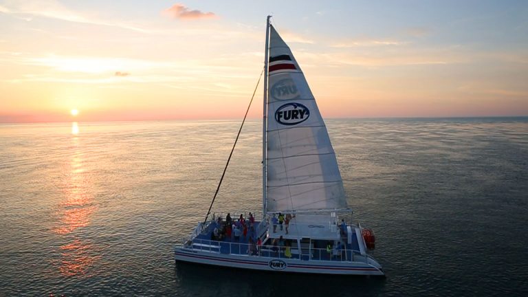 Aerial view of Fury Catamaran sailing the ocean and carrying guests with Key West sunrise on the horizon