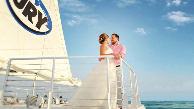 Picture of a Fury catamaran with a wedding couple looking at and smiling at each other and the ocean behind them.
